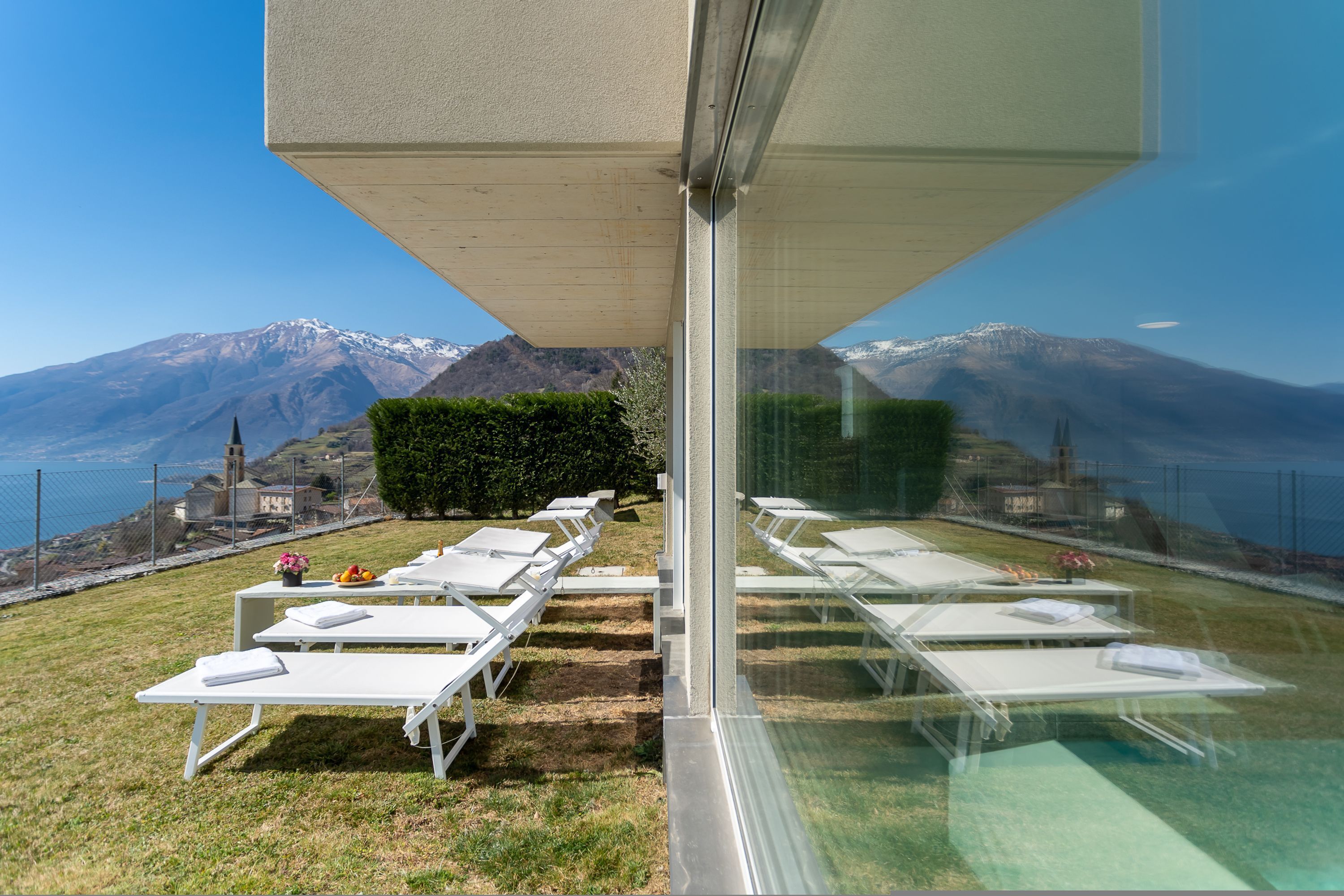 A terrace with sun loungers, a hedge, and a mountain view.