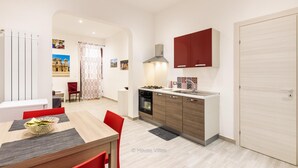 A compact kitchen with a stove, sink, and red cabinets. There is a dining area with a table and chairs, and a door leading to another room.