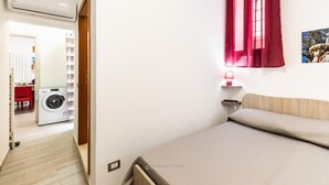 A bedroom with a bed, a wall-mounted lamp, and a red curtain.