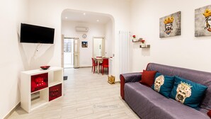 A modern living room with a sofa, a TV, and a dining area in the background.