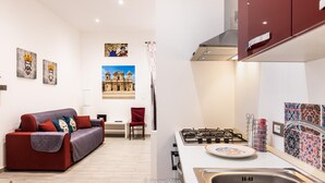 A modern living room with a sofa and a dining area. There is a kitchen with a stove and a sink.