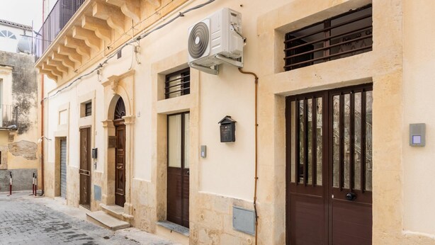 A building with a traditional architectural style, featuring a central entrance with a wooden door, a small mailbox, and a security system.