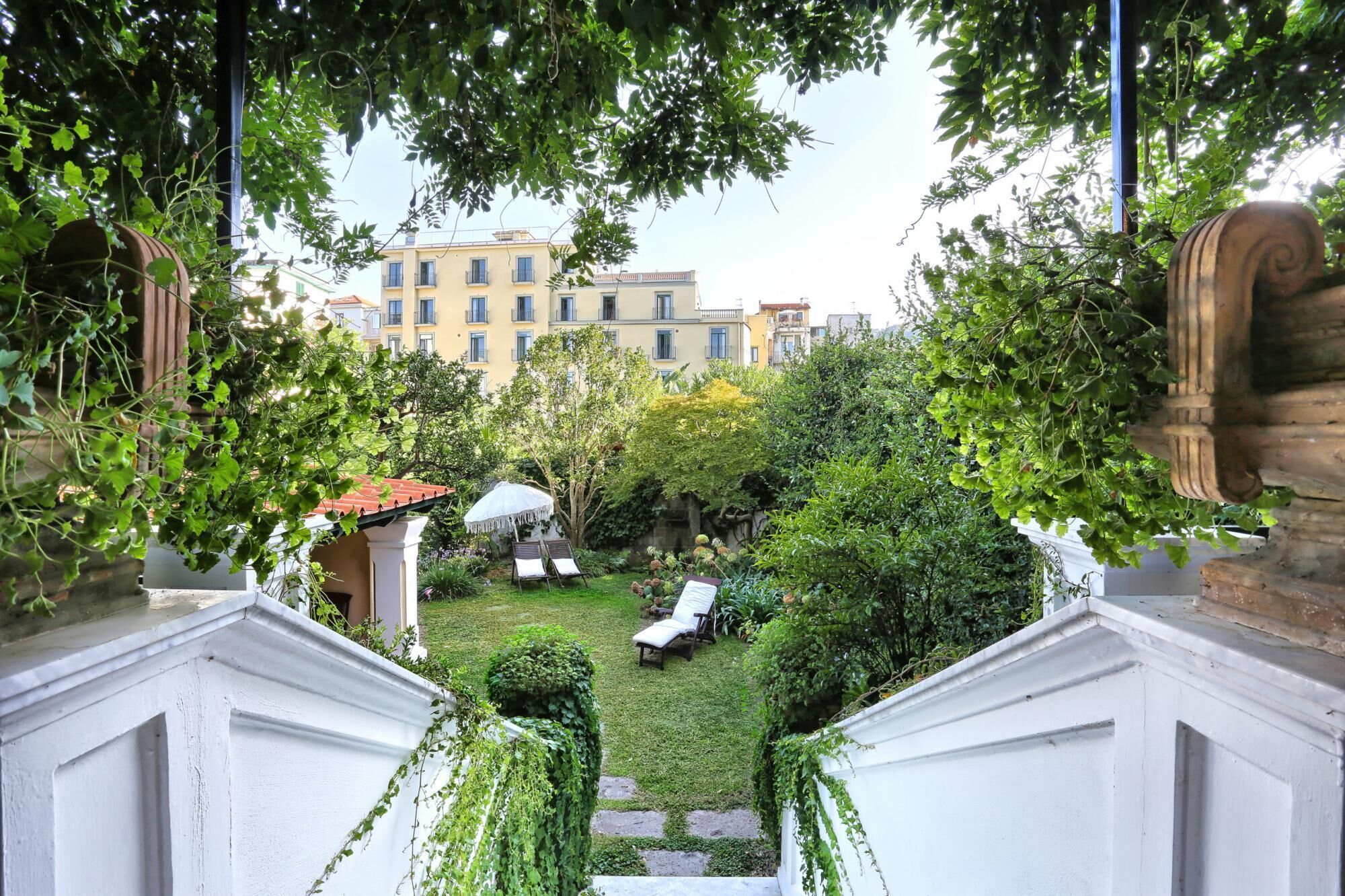 A courtyard with a small garden, a pergola, and a view of a multi-story building in the background.