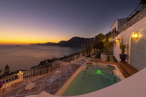 Eine Dachterrasse mit Whirlpool, Sitzgelegenheiten im Freien und Blick auf das Meer bei Sonnenuntergang.