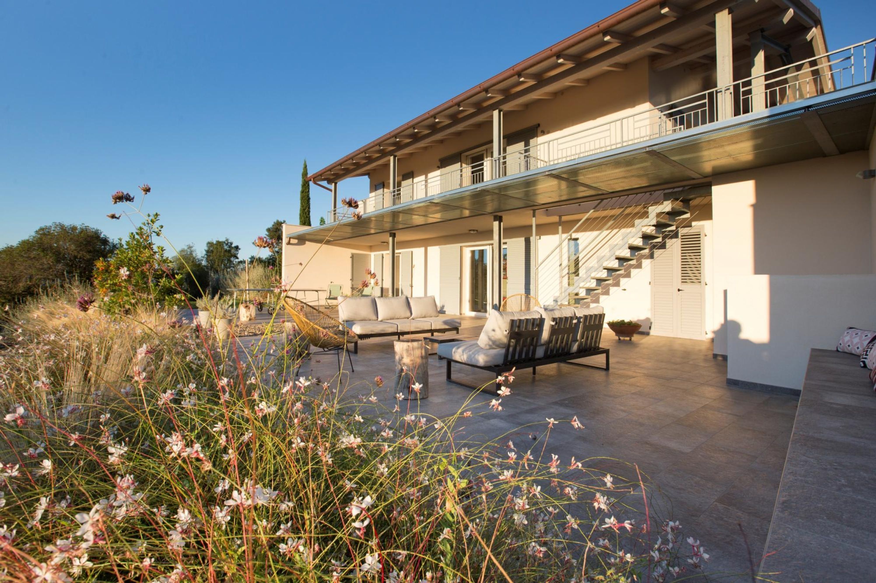 A modern house with a glass balcony, outdoor seating area, and a staircase leading to the upper floor.