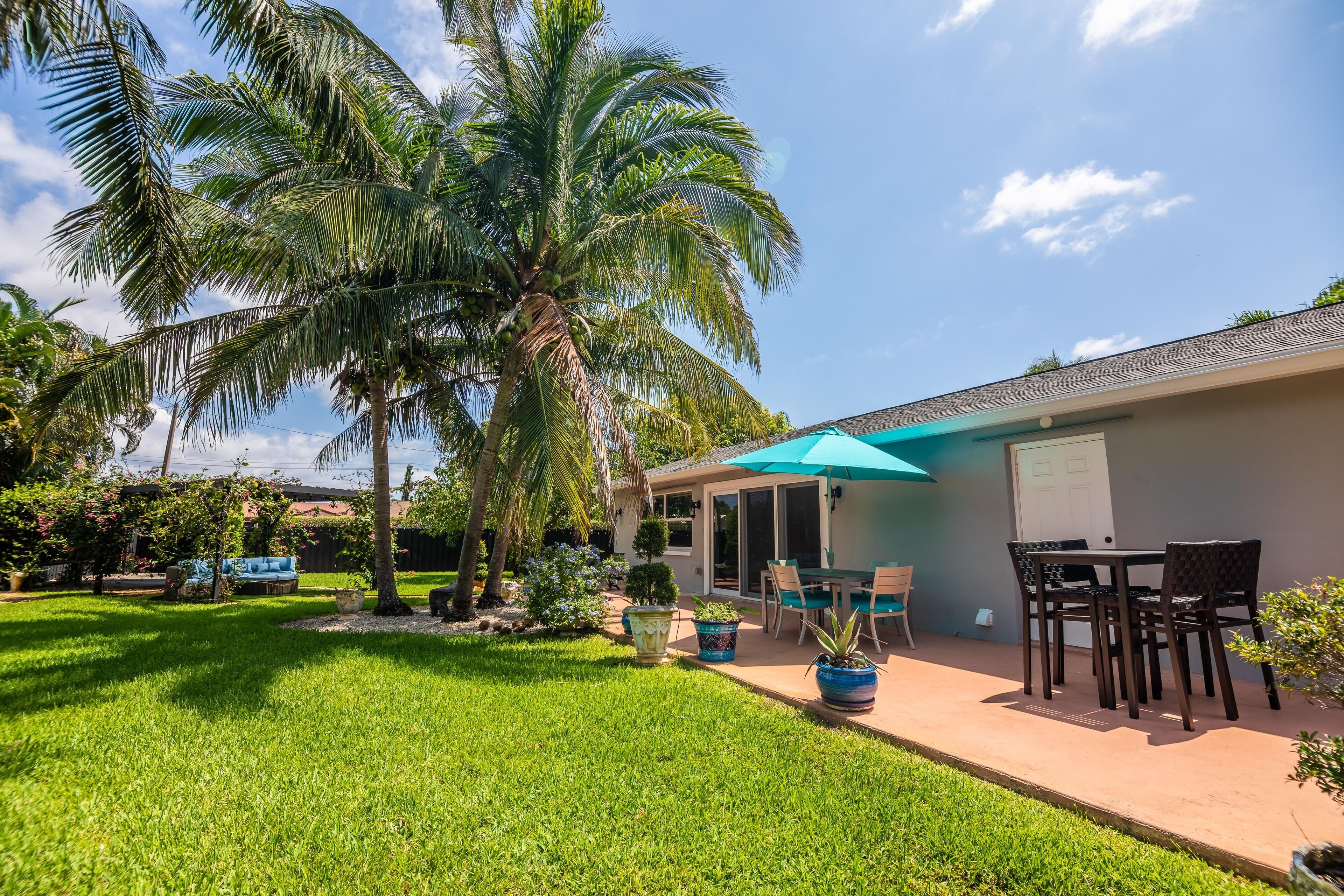 Un patio trasero con terraza, palmeras y una zona de estar techada.