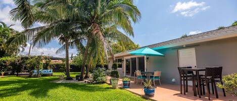 Un patio trasero con terraza, palmeras y una zona de estar techada.
