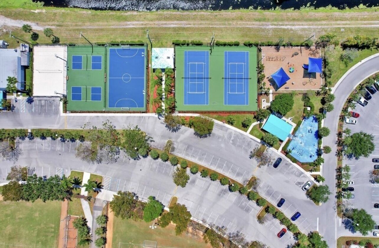 Eine Luftaufnahme eines Sportkomplexes mit mehreren Tennisplätzen, einem Schwimmbad und einem Parkplatz.