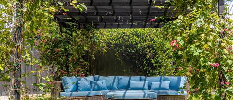 Un jardín con un sofá de mimbre y una pérgola cubierta de plantas trepadoras.