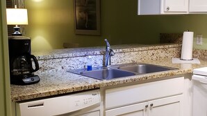 Una cucina con mobili bianchi, un piano di lavoro in granito, un lavello in acciaio inossidabile, una macchina per il caffè e una lavastoviglie.