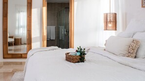 A bedroom with a large mirror, a wicker basket with toiletries, and a bed with white bedding. - New York Times featured this Beachfront Penthouse w/Dior inspired Rooftop & Pool (Las Terrenas)