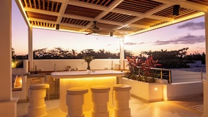 A modern outdoor kitchen with a bar area, seating, and a view of the sunset. - New York Times featured this Beachfront Penthouse w/Dior inspired Rooftop & Pool (Las Terrenas)