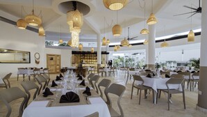 A spacious dining area with multiple tables set for guests, featuring a modern chandelier and a large window offering a view of the outdoors. - New York Times featured this Beachfront Penthouse w/Dior inspired Rooftop & Pool (Las Terrenas)