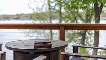 Een houten terras met een ronde tafel en stoelen, met uitzicht op een waterpartij met bomen op de achtergrond.