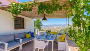 An outdoor patio with a table and chairs, a sofa, and a pergola with vines. - Casa de Juanito Viñuela by Ruralidays (Málaga)