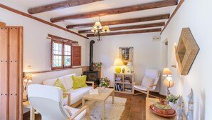 A cozy living room with a fireplace, white sofas, wooden beams, and a bookshelf. - Casa de Juanito Viñuela by Ruralidays (Málaga)