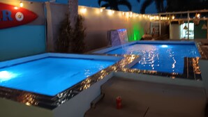 Een zwembad met een waterattractie en sfeerverlichting.