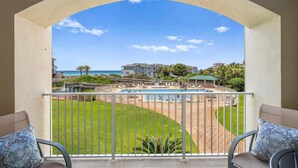 A balcony with a view of a swimming pool, a grassy area, and a building in the background. - Comfy 1-Bedroom, 2-Bath Condo in Gated Community - Includes 3 Adult Bikes! (Santa Rosa Beach)