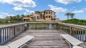A waterfront property with a wooden deck, lounge chairs, and a large house with multiple stories and a balcony. - Comfy 1-Bedroom, 2-Bath Condo in Gated Community - Includes 3 Adult Bikes! (Santa Rosa Beach)