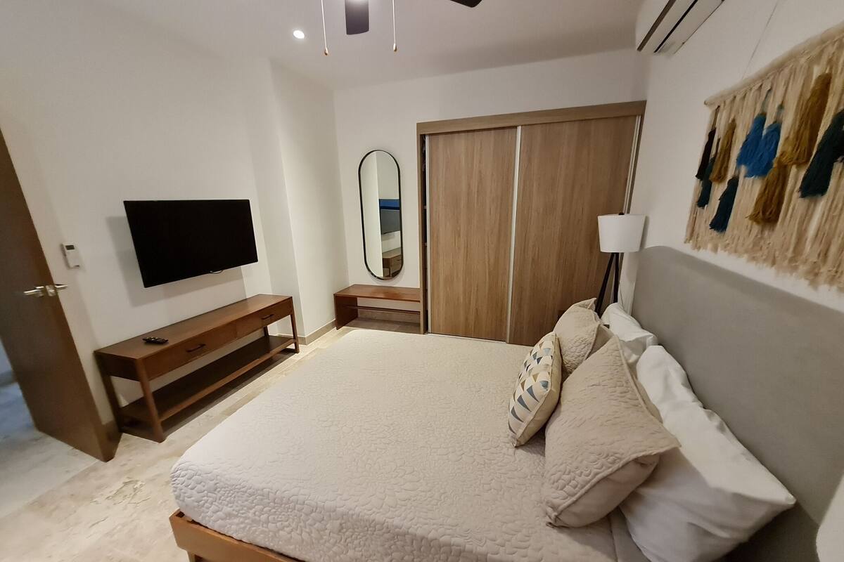 A bedroom with a bed, a TV, a mirror, a wardrobe, and a bedside lamp.