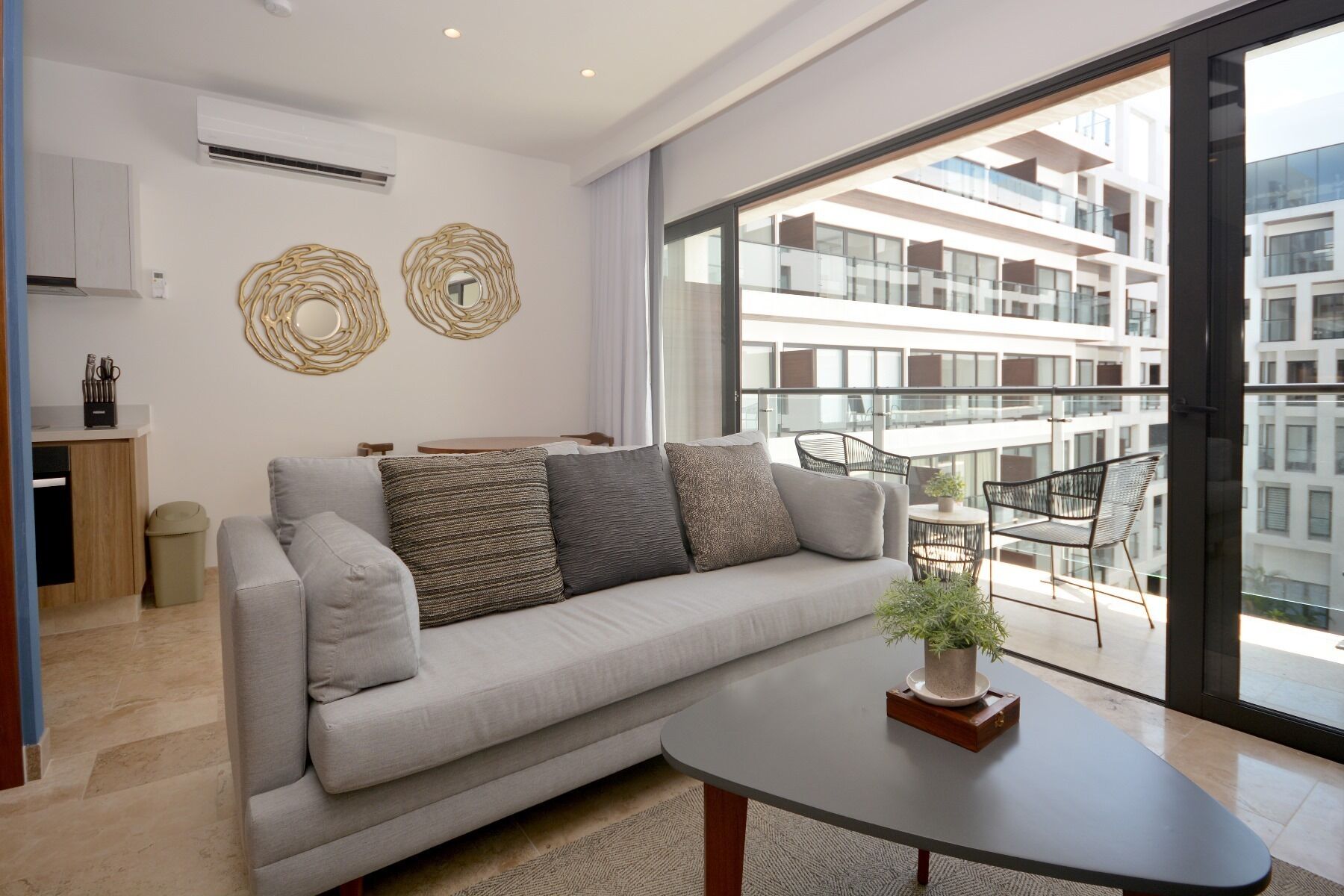 Uma sala de estar moderna com um sofá cinzento, uma mesinha redonda com uma planta e uma varanda com mobiliário para exterior.