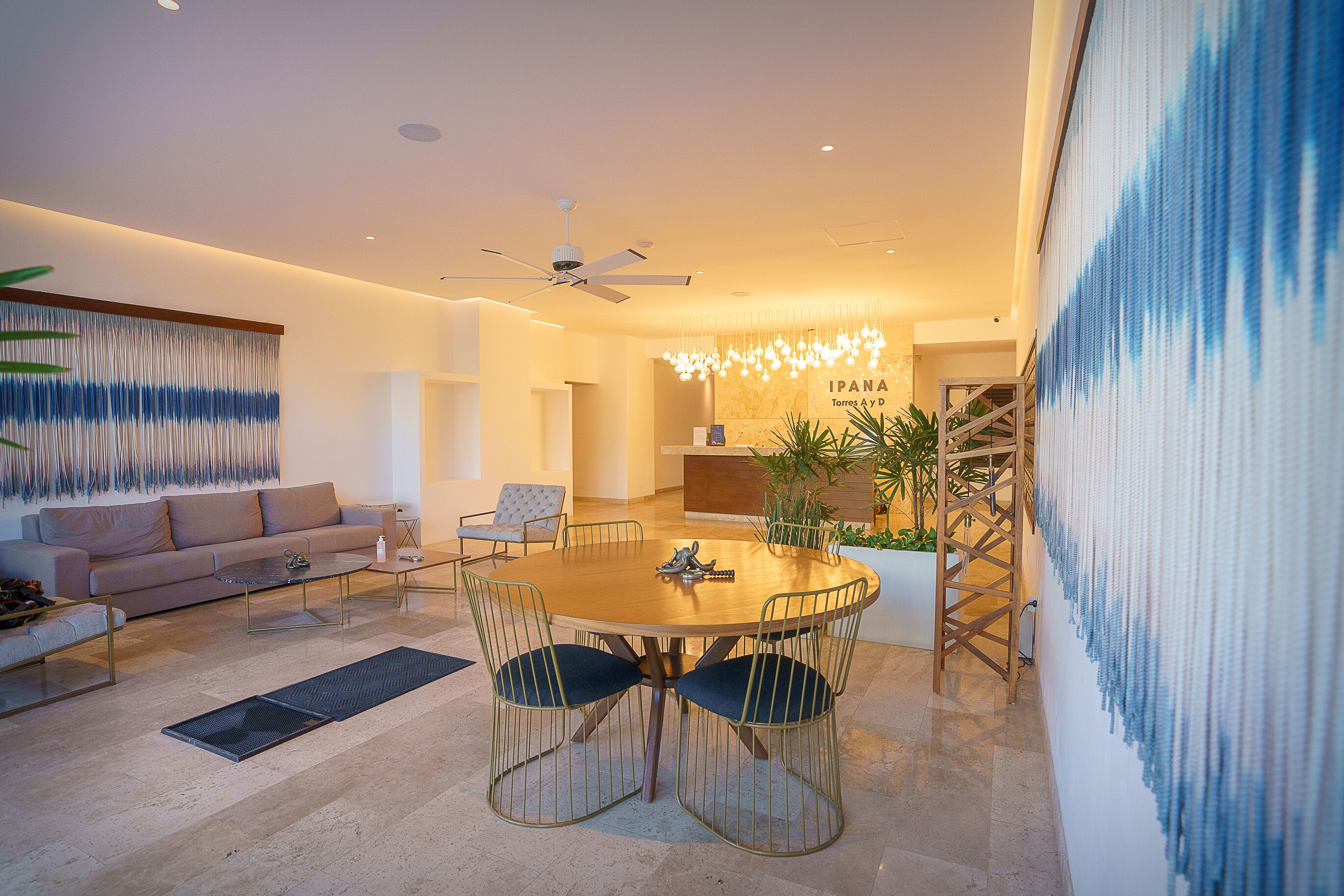 Un salon moderne avec une table à manger ronde, des sièges confortables, un ventilateur de plafond et un grand tableau abstrait accroché au mur.
