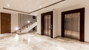 A modern lobby with a marble floor, a staircase with vertical lines, and two elevators. - Ipana Apartment Deluxe (Playa del Carmen)