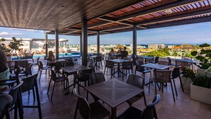 An outdoor patio with tables and chairs, overlooking a swimming pool and a cityscape. - Ipana Apartment Deluxe (Playa del Carmen)