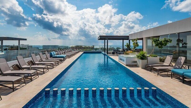 A rooftop infinity pool with lounge chairs, a covered seating area, and a view of the city skyline. - Ipana Apartment Deluxe (Playa del Carmen)