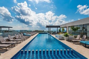 A rooftop infinity pool with lounge chairs, a covered seating area, and a view of the city skyline. - Ipana Apartment Deluxe (Playa del Carmen)