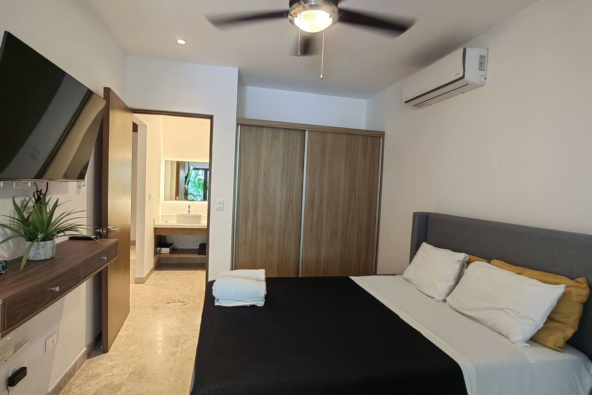 A modern bedroom with a bed, a TV, a ceiling fan, and a wardrobe.