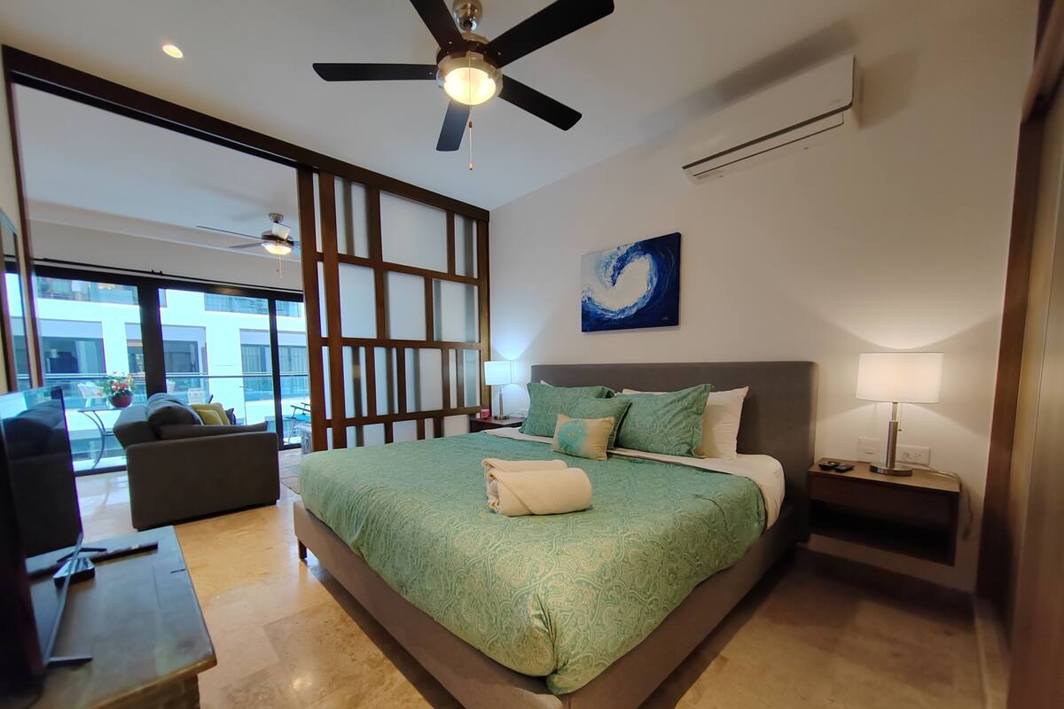 A spacious bedroom with a large bed, a ceiling fan, a view of the outdoors, and a painting on the wall.