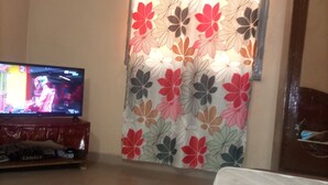 Een kamer met een televisie op een houten standaard, een bed met een witte matras en een bloemenprint gordijn.