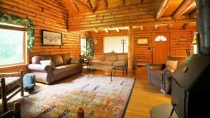A cozy log cabin interior with a fireplace, a sofa, a loveseat, and a patterned rug.