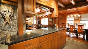 A log cabin interior with a stone fireplace, wooden cabinetry, and a dining area with a chandelier.