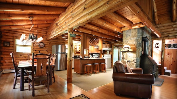 A log cabin interior with a dining area, kitchen, and a fireplace.