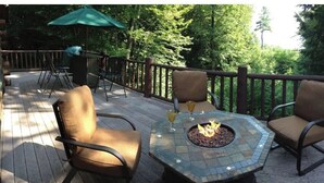 An outdoor deck with a fire pit table, two chairs, and a table with drinks.