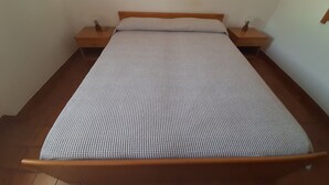 Une chambre avec un lit simple, une tête de lit en bois, une couvre-lit à carreaux et deux tables de chevet avec des lampes.