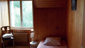 Una habitación de cabaña de madera con una cama, una silla, una mesa y una ventana.