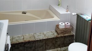 Un baño con bañera, inodoro y un pequeño estante con artículos de aseo.