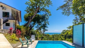 Una piscina con vista sull'oceano, immersa nel verde e affiancata da un edificio con un balcone.