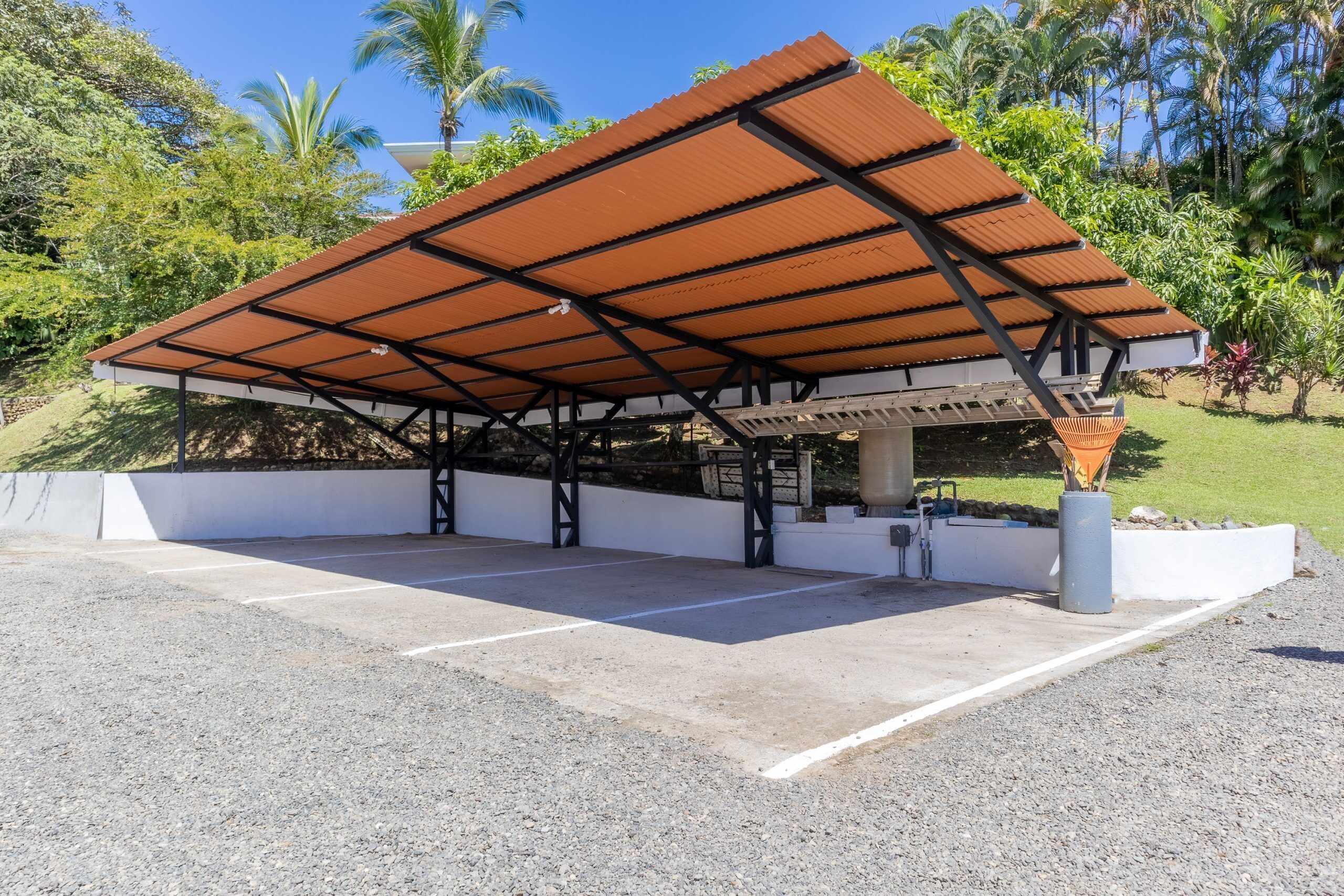 A covered parking area with a metal roof, concrete floor, and a white wall.