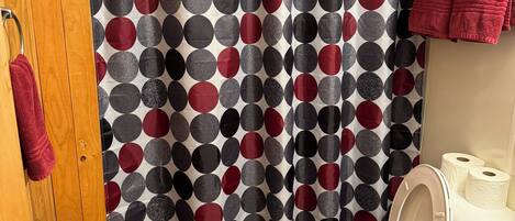 Une salle de bain avec un rideau de douche à pois, des toilettes et un tapis noir.