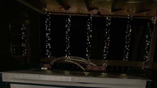 Un jacuzzi con panel de control, rodeado por una terraza de madera y luces colgantes.