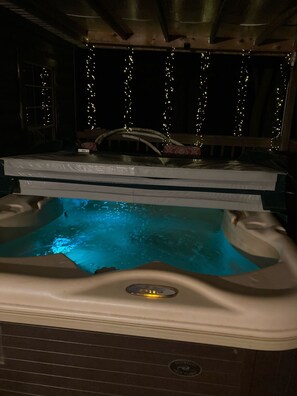 Un jacuzzi con panel de control, rodeado por una terraza de madera y luces colgantes.