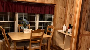 Una habitación con paneles de madera, una mesa de comedor, sillas, un jarrón con flores y una estantería con objetos.