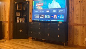 Habitación con paneles de madera y un televisor de pantalla plana grande que muestra la interfaz de Disney+.