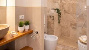 Ein modernes Badezimmer mit einer großen Badewanne, einem Waschbecken und einer Toilette. Auf dem Regal über dem Waschbecken stehen zwei Blumentöpfe.