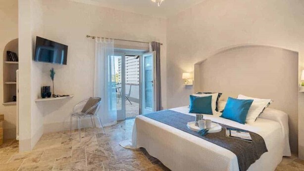 Ein Schlafzimmer mit Bett, Fernseher, Sessel und Balkontür.