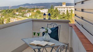 Ein Balkon mit Tisch, zwei Stühlen, einem Buch, einer Blumenvase und zwei Getränken.